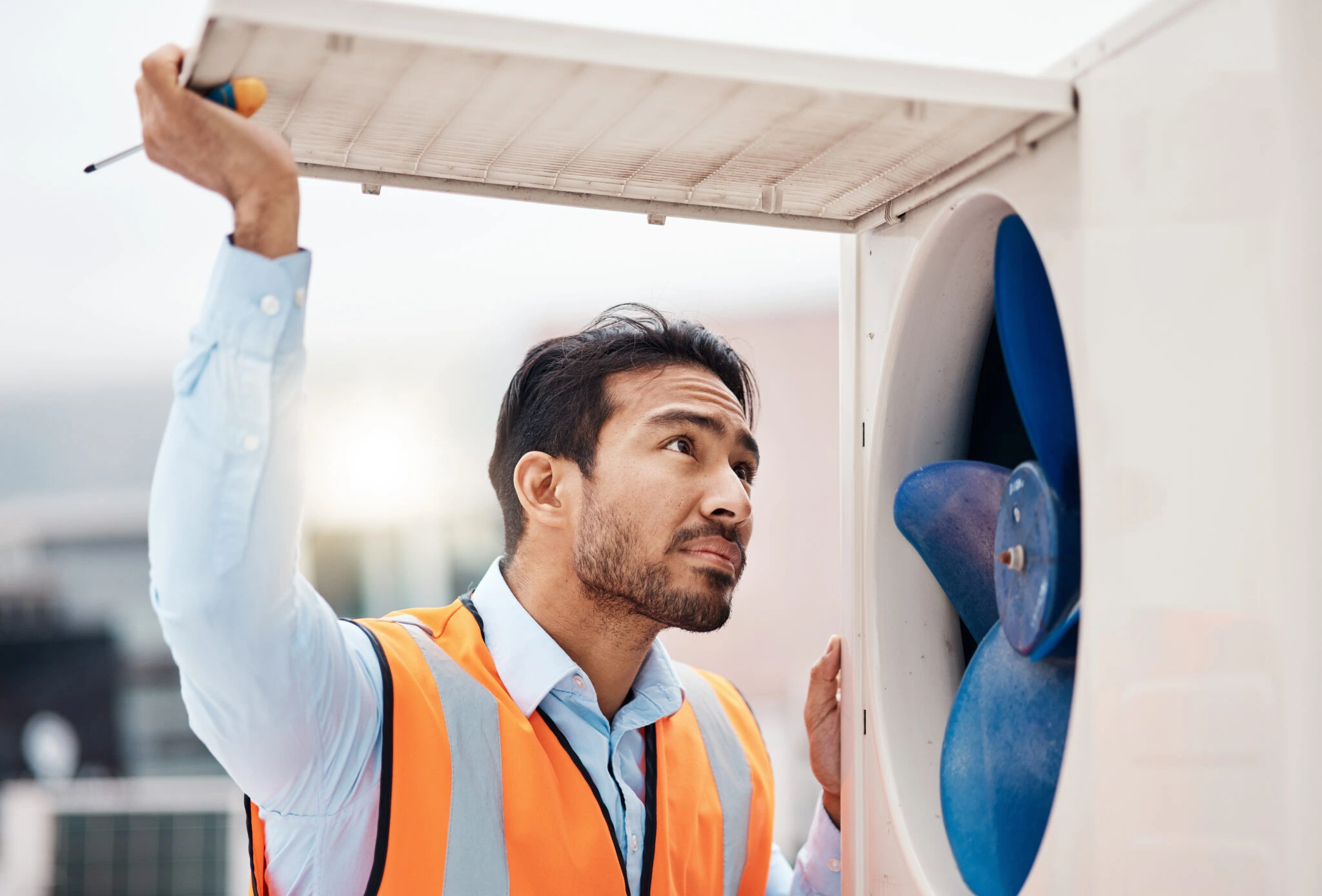 a man in an orange vest looking at AC outdoor unit